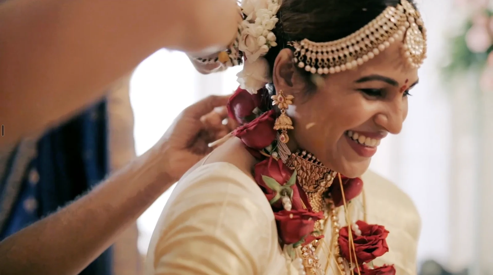 A bride smiling as her wedding jewellery is fastened